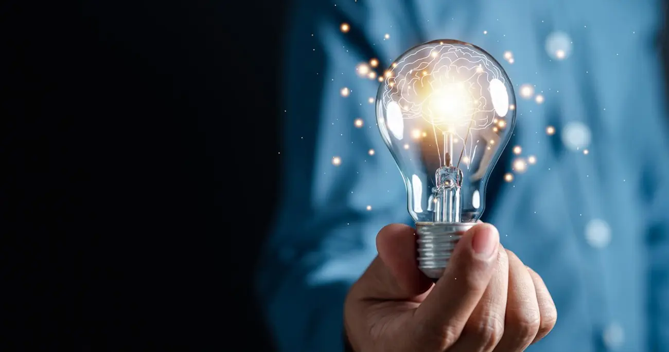 En hand håller en lysande glödlampa med konturerna av en hjärna inuti.