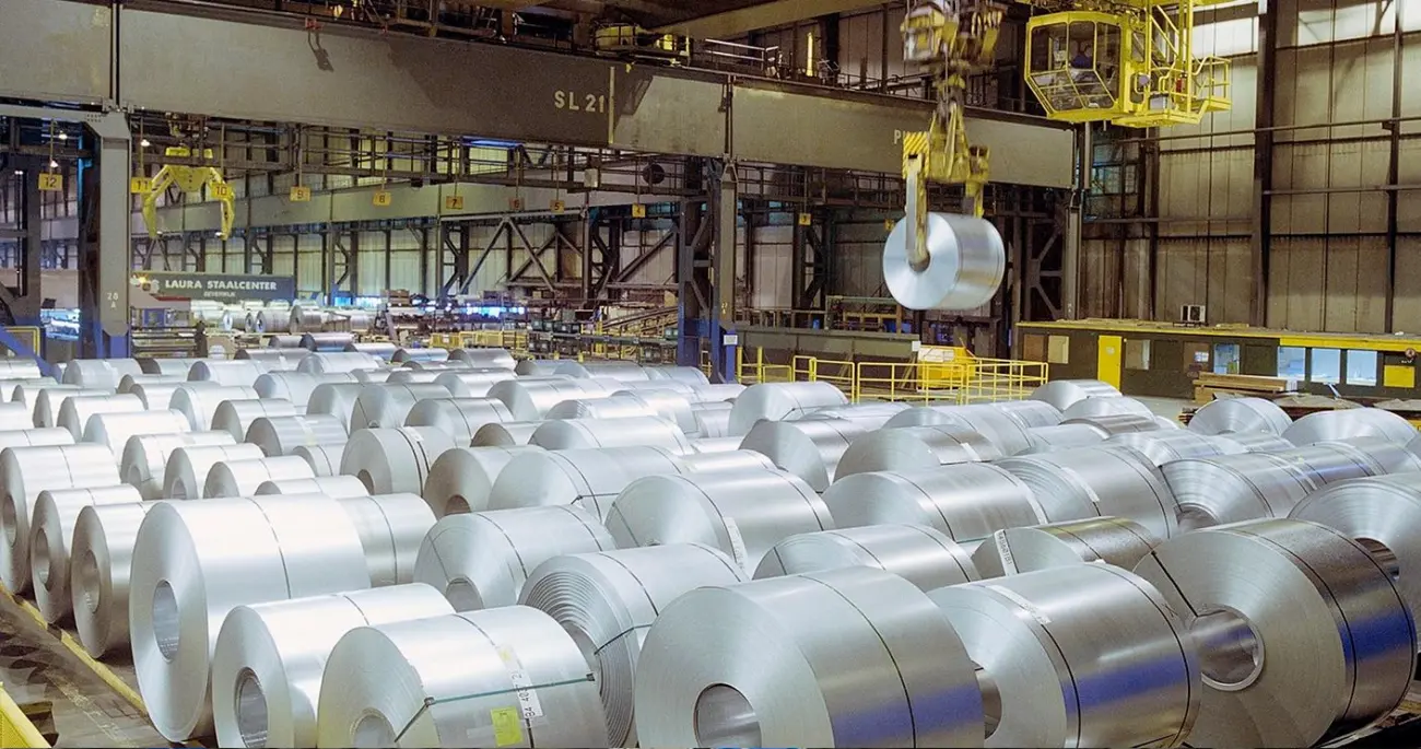 Stahlcoils in einer Industriehalle, in der ein Brückenkran einen Coil anhebt.