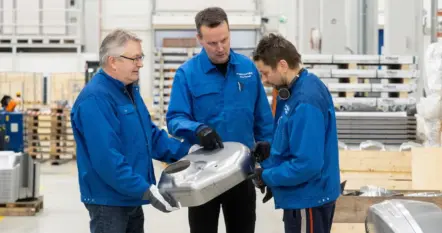 Drei Mitarbeiter von Meconet betrachten eine große geformte Metallkomponente in der Produktion.