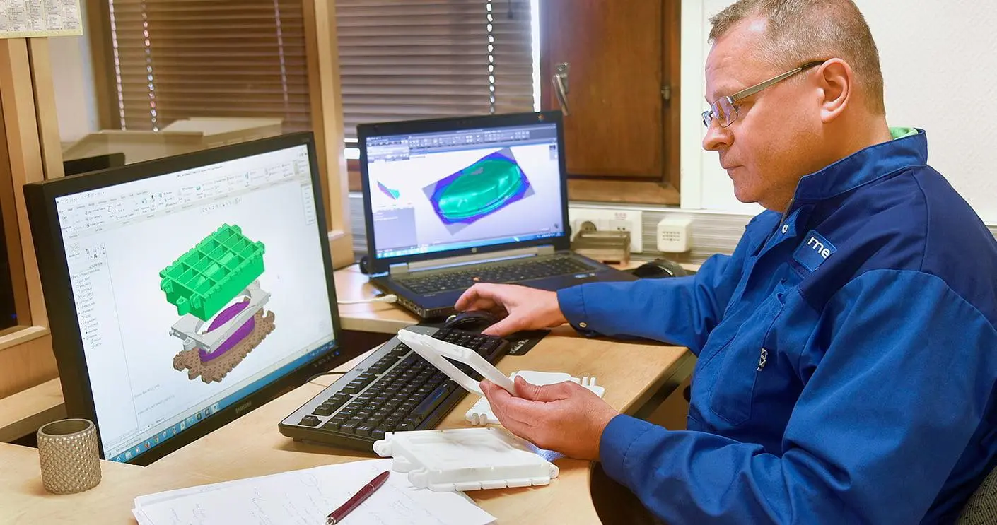En konstruktör håller en skalmodell; skärmarna visar en 3D-modell av ett verktyg och en formningssimulering.