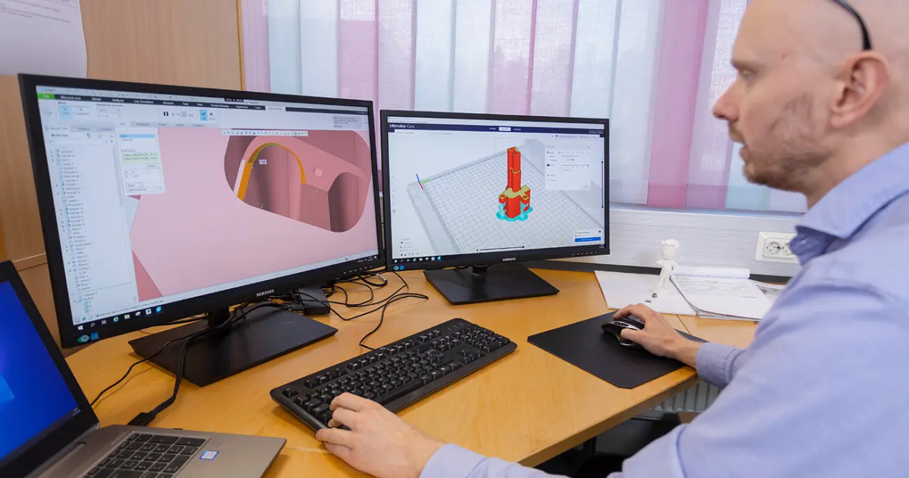 A designer works with 3D models of parts displayed on two monitors.