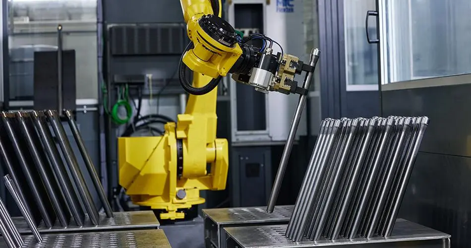 A yellow industrial robot handling a long metal component beside a machine tool.
