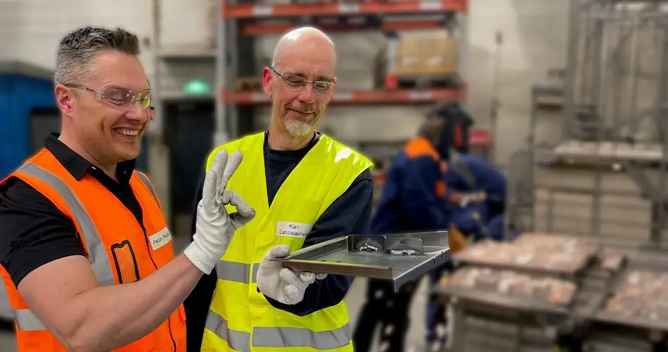 Kaksi henkilöä tarkastelee metallikomponenttia tuotantotiloissa.